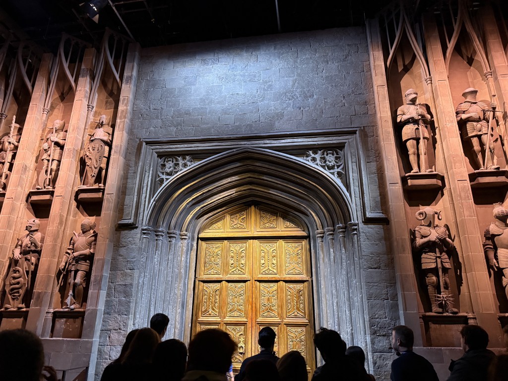 Prikaz ulaznih vrata Velike dvorane iz Warner Bros. Studija u Londonu, okruženih kamenim zidovima i statue likova iz filma.